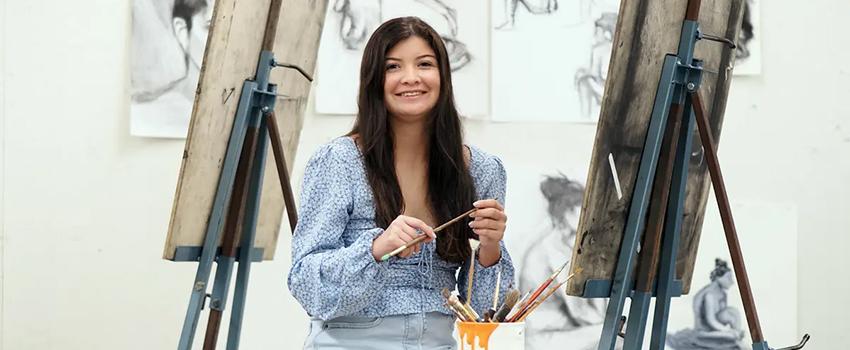 Honors student in paint studio holding a paint brush.